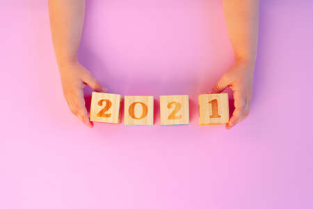Hands of a kid holding 2021 Year wooden cubes on pink backgroundの写真素材