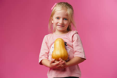 Little girl holding pumpkin in her hands against pink backgroundの写真素材