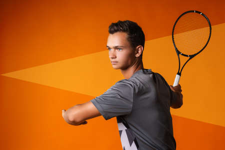 Portrait of a young man tennis player on orange backgroundの写真素材