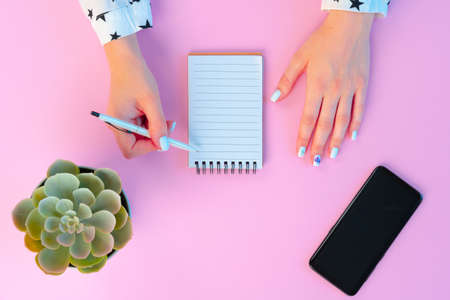 Female hands and open notepad on pink background