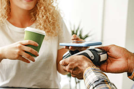 Woman customer of coffee shop paying for coffee through mobile phone using contactless technologyの写真素材