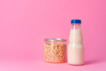Oat milk in glassware and dry oat flakes on pink background