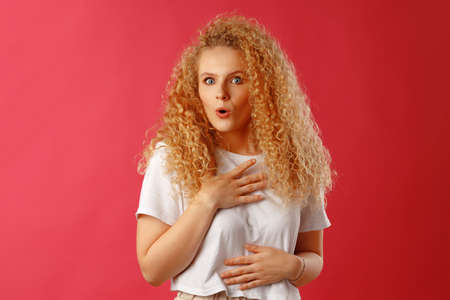Shocked and amazed young curly woman against pink background