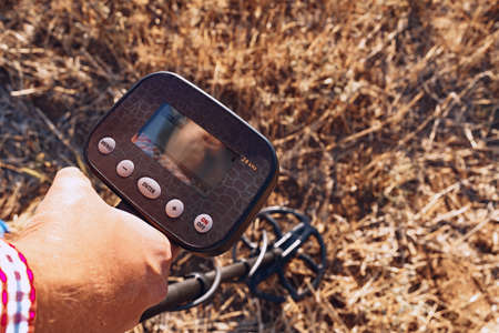 Male hand holding metal detector device above the groundの写真素材