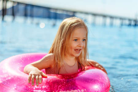 Little girl with pink inflatable circle bathing in sea