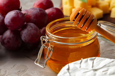 Cheese served with grapes and honey on grey surface