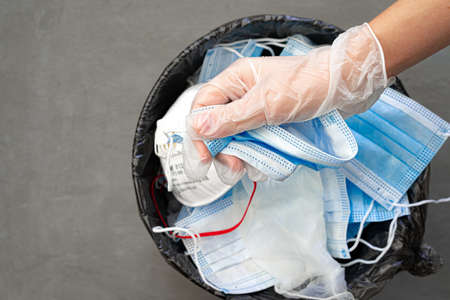 Hand putting used dirty surgical mask to a garbage bin.