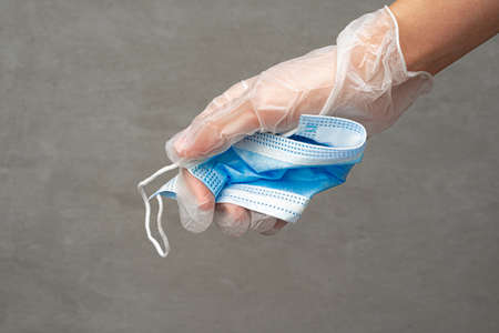 Hand putting used dirty surgical mask to a garbage bin.