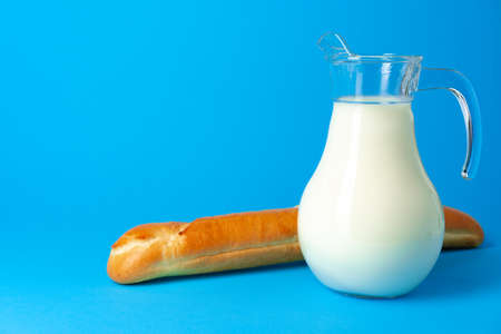 Fresh baguette bread and pitcher with fresh milk on blue backgroundの写真素材