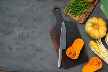 Small pumpkin cut into halves on wooden cutting board with knife