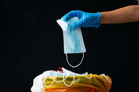 Hand putting used dirty surgical mask to a garbage bin.