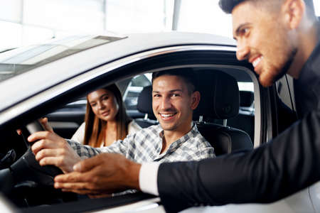 Young couple choosing a car at the dealership with manager helping