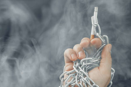 Male hand in metal chains holding cigarette