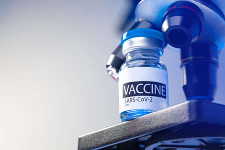 Vial of Covid-19 vaccine next to a microscopeの写真素材