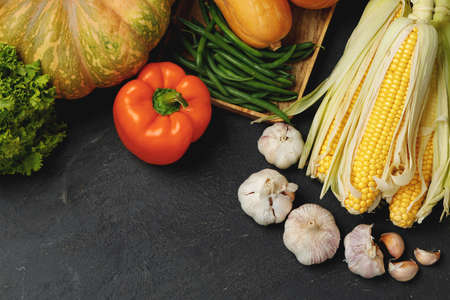 Autumn vegetable composition with pumpkin, corn and pepper on black background