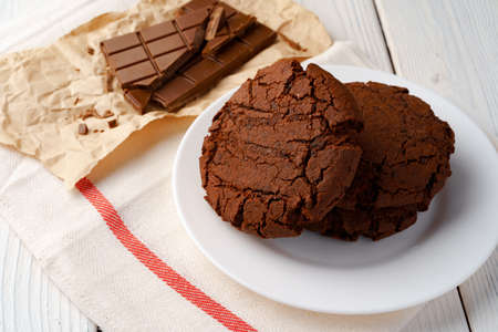 Chocolate cookies and chocolate bar on white wooden board