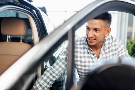 Cheerful young man customer buys a new car in a dealership