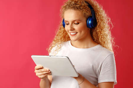 Positive young woman standing with blue headphones against pink background