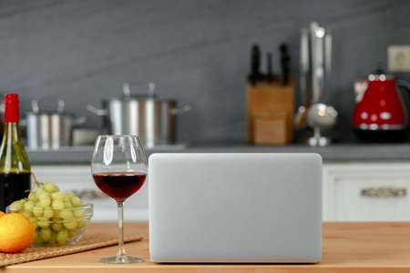 Laptop and glass of red wine on wooden kitchen tableの写真素材