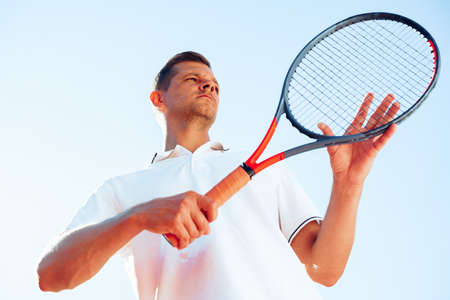 Young man tennis player checks his racket to start a gameの写真素材