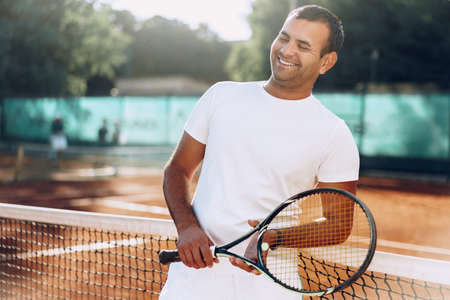 Spoty man with tennis racket standing on clay court near netの写真素材