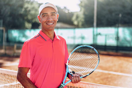 Middle-aged man tennis player with racket standing on court near netの写真素材