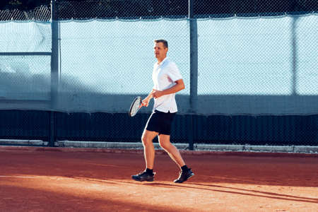 Young man plays tennis outdoors on tennis court in the morningの写真素材