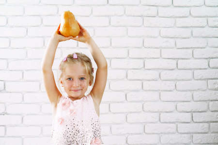 Cute little girl in pink dress holding pumpkin in her handsの写真素材