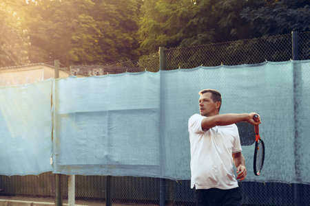 Young man plays tennis outdoors on tennis court in the morning