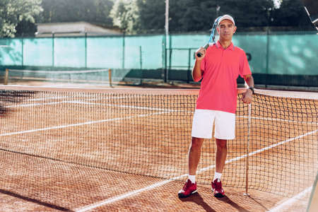 Middle-aged man tennis player with racket standing on court near netの写真素材