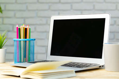 Open laptop with notepad and heap of pencils on wooden desk