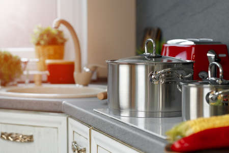 Still life photo of metal casseroles on induction stove in kitchen
