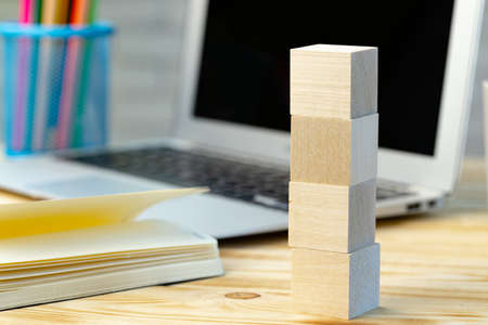 Stacked four wooden blocks on working desk with open laptop and bookの写真素材