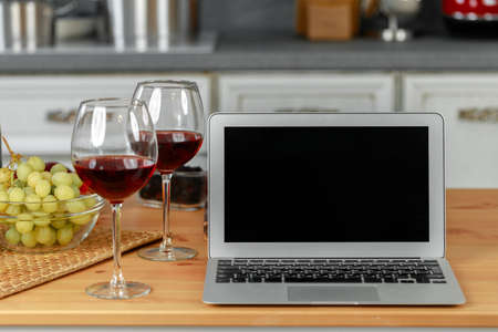 Laptop and glass of red wine on wooden kitchen tableの写真素材