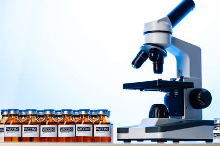 Vial of Covid-19 vaccine next to a microscopeの写真素材