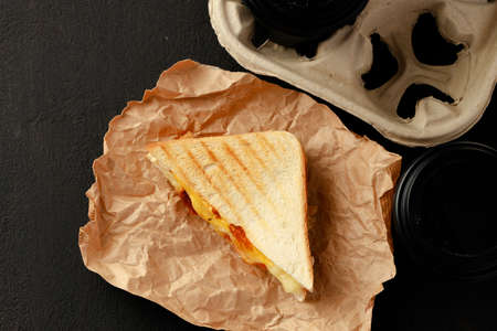 Toasted sandwich in craft paper with cup of coffee on tableの写真素材