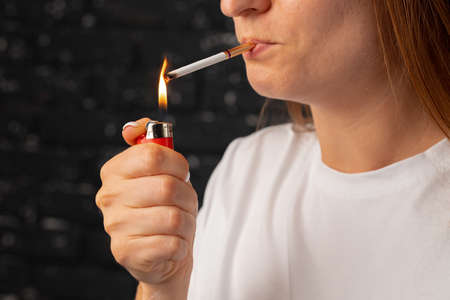 Unrecognizable woman lights cigarette with fire lighterの写真素材