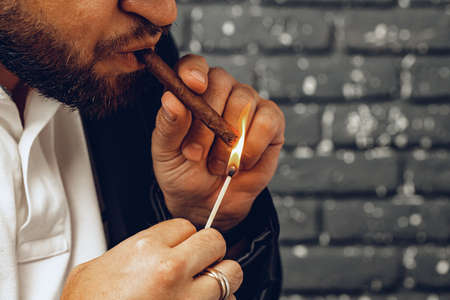 Bearded man smoking cigar against black brick wallの写真素材