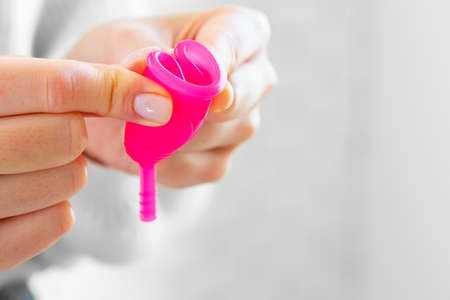 Woman in white sweater holding pink menstrual cup in hands close upの写真素材