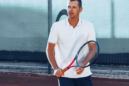 Young man plays tennis outdoors on tennis court in the morning