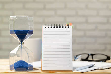 Open notepad page and hourglass on wooden working deskの写真素材