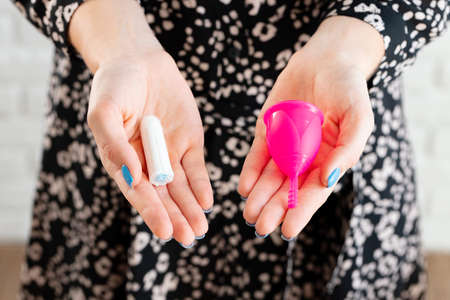 Female hands holding menstrual cup and medical tampon