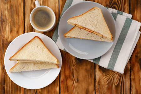 Toast sandwich and cup of coffee on napkin on wooden table