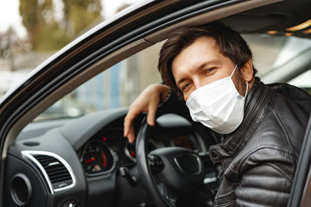 Young man driving car in medical maskの写真素材
