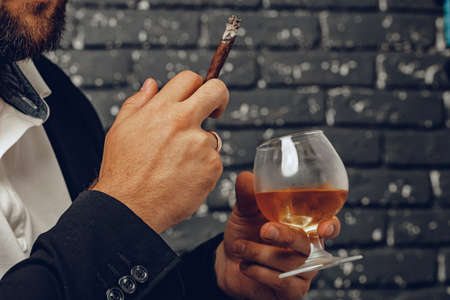 Man holding a glass of whisky and lit cigarette in hands close upの写真素材