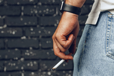 Male hand holding lit cigarette against black backgroundの写真素材