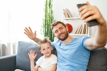Father and son making a video call on smartphone while sitting on couchの写真素材