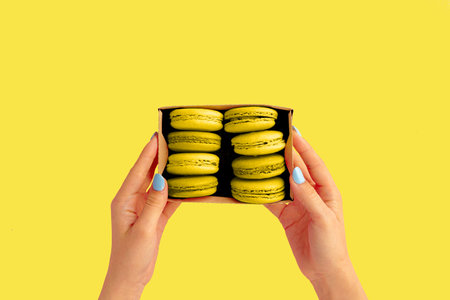 Womans hands holding box with illuminatingyellow macaroon cookies.の写真素材