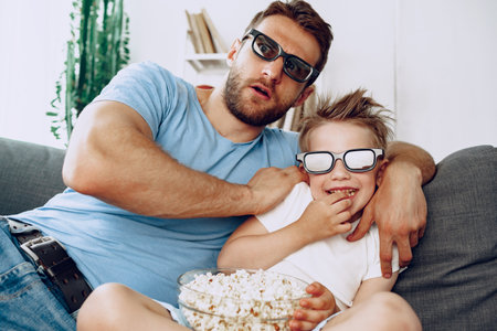 Father and son watching movies at home in 3d glasses and eating popcornの写真素材