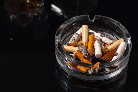 Ash tray full of cigarette butts on black backgroundの写真素材